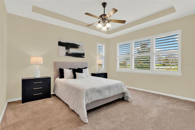 bedroom with a tray ceiling, light carpet, baseboards, and ceiling fan