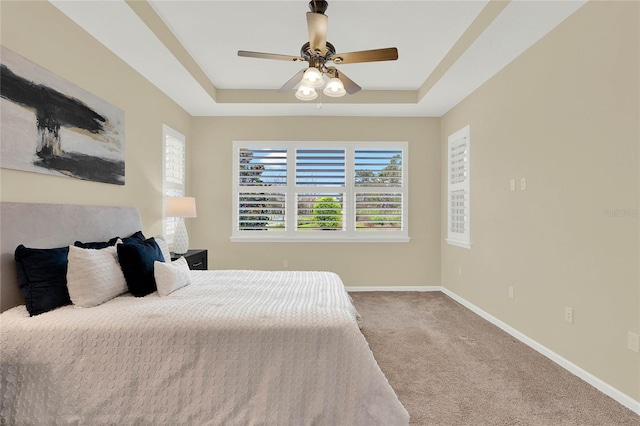 carpeted bedroom featuring multiple windows, a raised ceiling, and baseboards