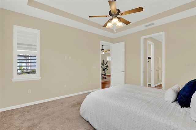 carpeted bedroom featuring visible vents, a raised ceiling, baseboards, and ceiling fan