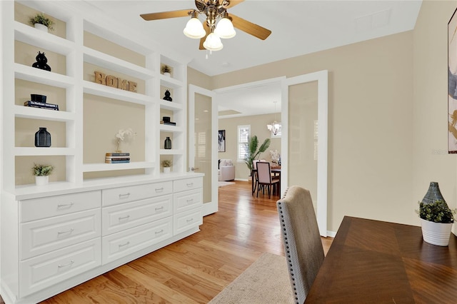 office with visible vents, built in shelves, baseboards, ceiling fan with notable chandelier, and light wood-style floors