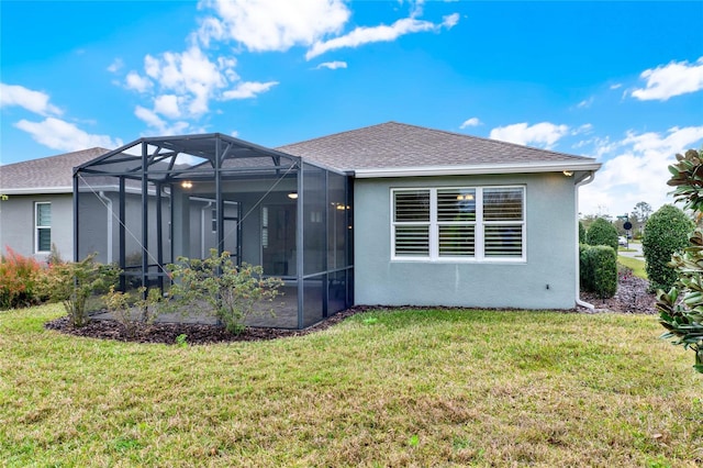 rear view of property with a yard, roof with shingles, glass enclosure, and stucco siding