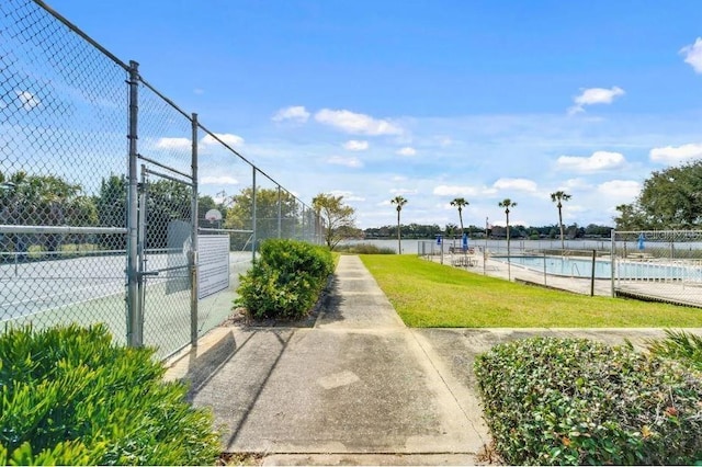 view of community with a swimming pool, a gate, fence, and a lawn