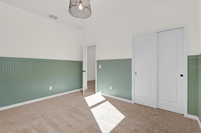 unfurnished bedroom with a wainscoted wall, a closet, visible vents, and carpet flooring