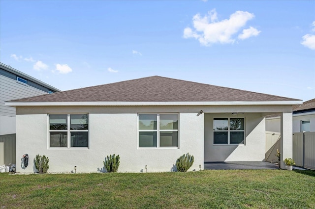 rear view of property with roof with shingles, fence, a lawn, and stucco siding