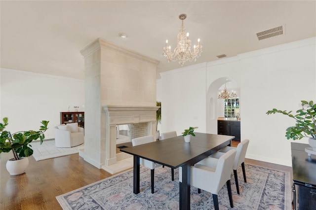 dining space with visible vents, arched walkways, ornamental molding, a tiled fireplace, and a chandelier