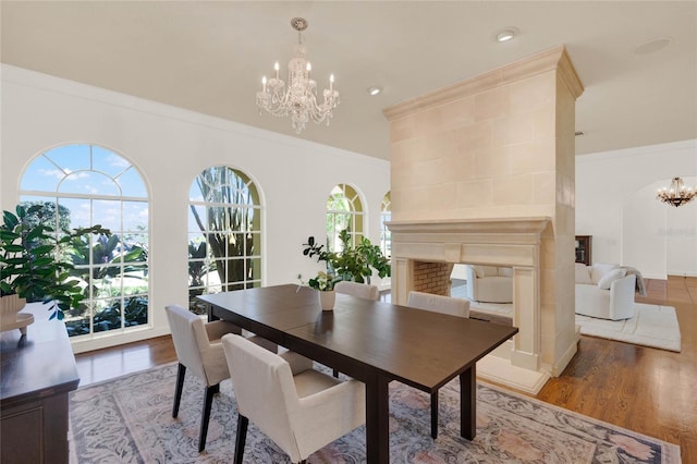 dining room featuring a multi sided fireplace, light wood finished floors, a chandelier, and ornamental molding