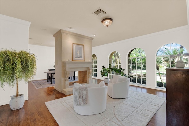 living area featuring visible vents, crown molding, baseboards, a multi sided fireplace, and wood finished floors