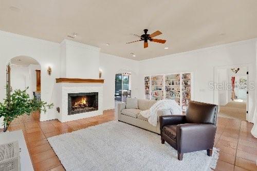 living area with ceiling fan, ornamental molding, and a lit fireplace