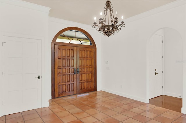 entryway featuring arched walkways, light tile patterned floors, crown molding, and baseboards