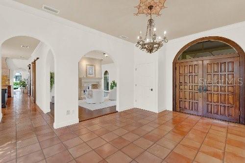 tiled entrance foyer with visible vents, arched walkways, baseboards, and crown molding