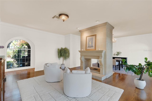 sitting room featuring a fireplace, wood finished floors, arched walkways, and ornamental molding