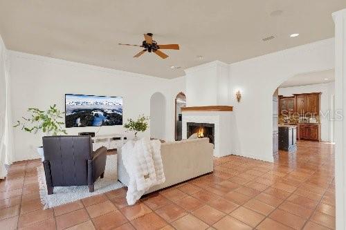 living room with a ceiling fan, arched walkways, and a lit fireplace