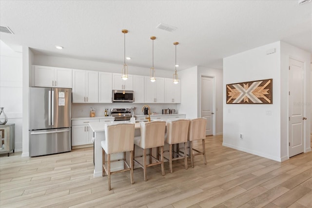 kitchen featuring an island with sink, light countertops, light wood-style flooring, a kitchen breakfast bar, and stainless steel appliances