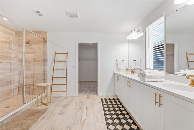 full bath featuring visible vents, a walk in closet, a sink, a shower stall, and double vanity