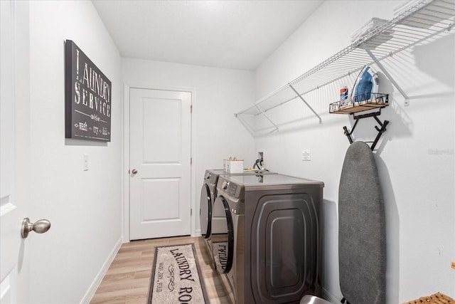 clothes washing area with laundry area, baseboards, light wood-style floors, and separate washer and dryer