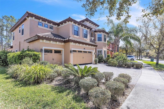 mediterranean / spanish-style house with a garage, a tiled roof, and stucco siding