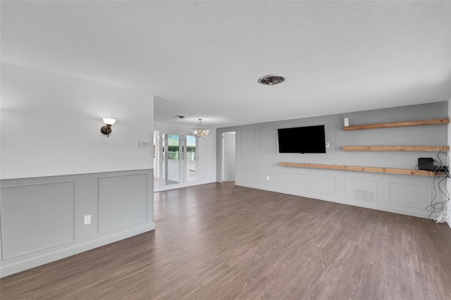 unfurnished living room featuring a textured ceiling, an inviting chandelier, wood finished floors, and a decorative wall