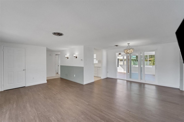 unfurnished living room with a notable chandelier, a textured ceiling, visible vents, and wood finished floors