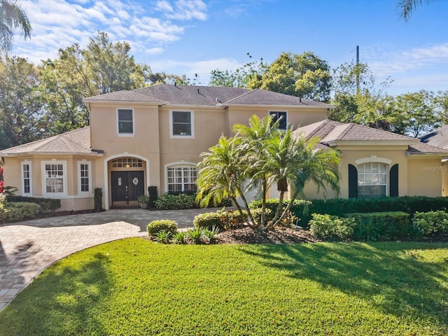 mediterranean / spanish home with stucco siding, a front lawn, and driveway