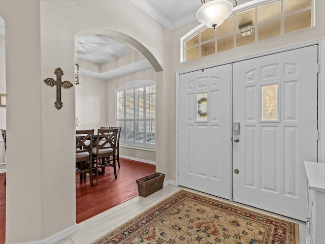 foyer with arched walkways, wood finished floors, baseboards, and ornamental molding