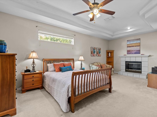 carpeted bedroom with a tiled fireplace, visible vents, and a tray ceiling