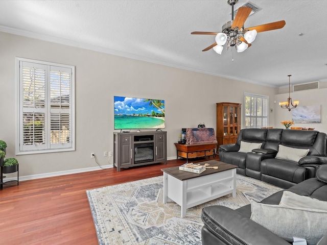 living room featuring ceiling fan with notable chandelier, wood finished floors, visible vents, and ornamental molding