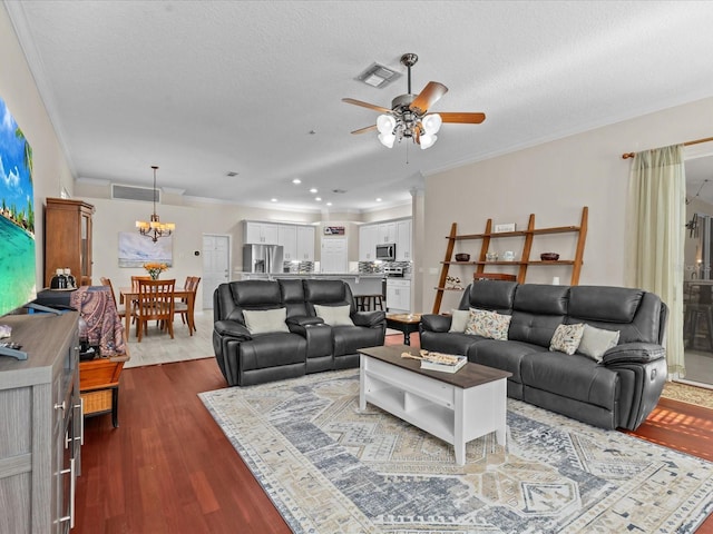 living area featuring crown molding, ceiling fan with notable chandelier, visible vents, and dark wood-style flooring