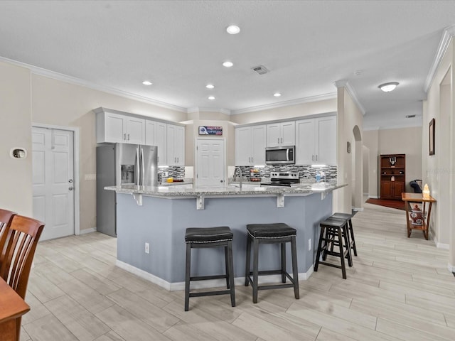 kitchen featuring light stone counters, visible vents, decorative backsplash, appliances with stainless steel finishes, and a kitchen bar