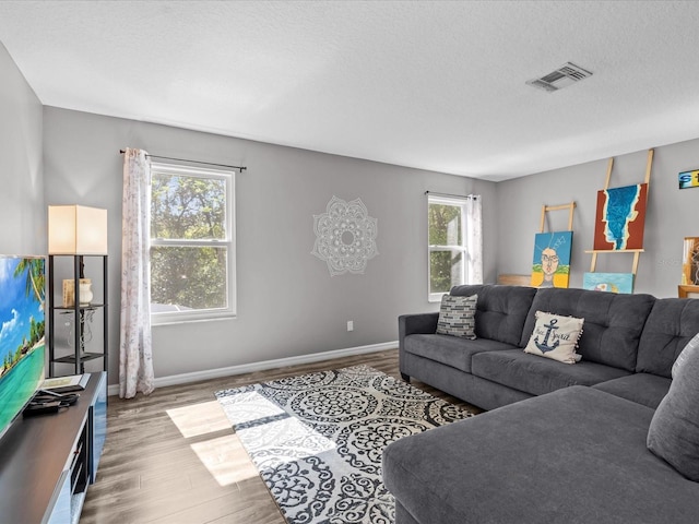 living room with visible vents, a textured ceiling, baseboards, and wood finished floors