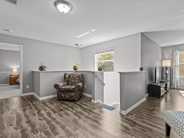 living area featuring an upstairs landing, a healthy amount of sunlight, a textured ceiling, and wood finished floors