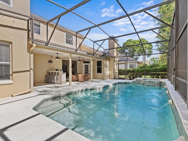 view of swimming pool featuring outdoor dry bar, a pool with connected hot tub, glass enclosure, ceiling fan, and a patio area