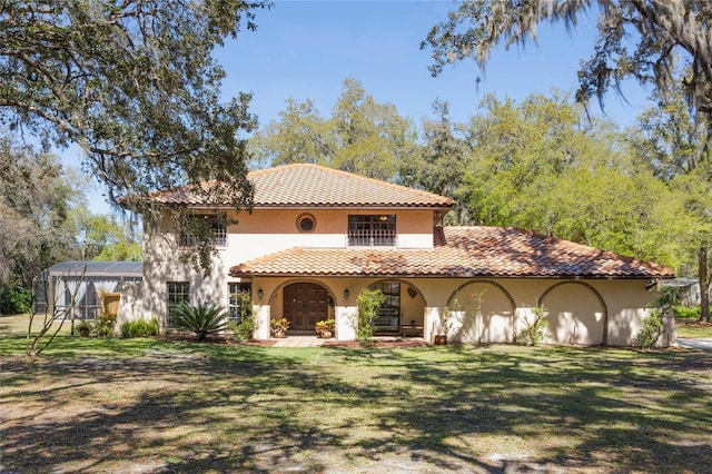 mediterranean / spanish house with stucco siding, a lanai, a front yard, and a tiled roof