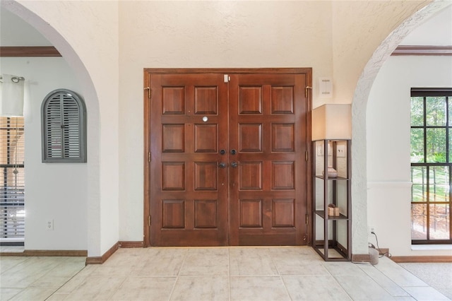 foyer entrance featuring light tile patterned floors, arched walkways, and baseboards