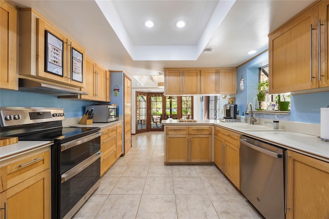 kitchen with under cabinet range hood, light countertops, a peninsula, stainless steel appliances, and a sink