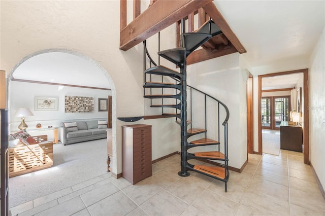 staircase with tile patterned floors, arched walkways, baseboards, and carpet floors