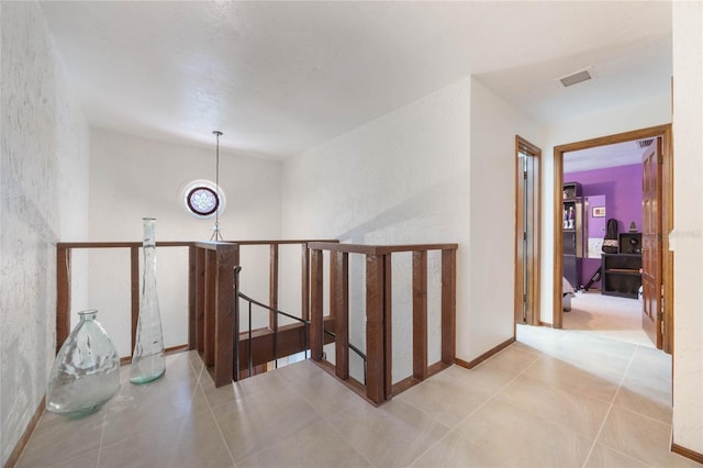 hall featuring tile patterned floors, visible vents, an upstairs landing, and baseboards