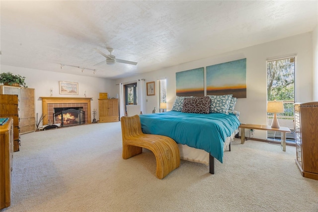 bedroom with a textured ceiling, ceiling fan, carpet flooring, and a tile fireplace