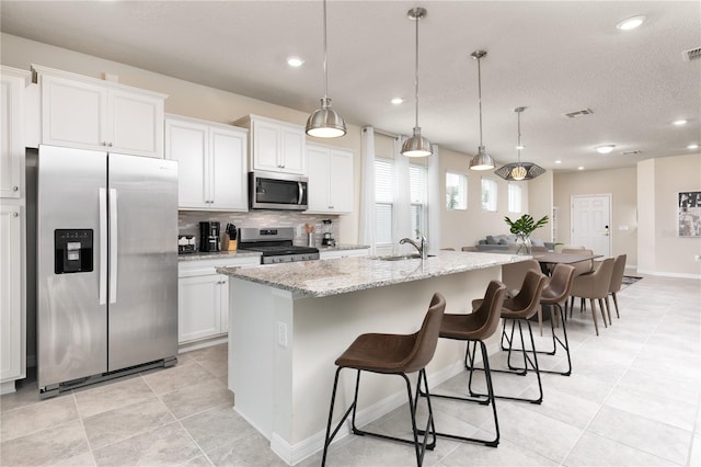 kitchen with visible vents, a center island with sink, a breakfast bar area, decorative backsplash, and appliances with stainless steel finishes