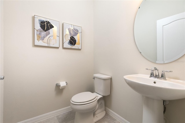 half bath with a sink, baseboards, toilet, and tile patterned flooring