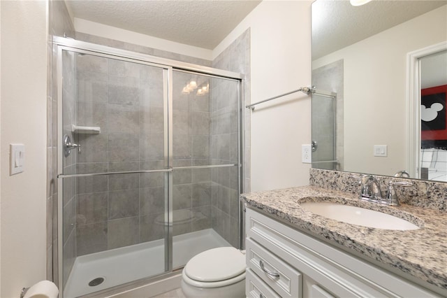 full bathroom featuring vanity, toilet, a stall shower, and a textured ceiling