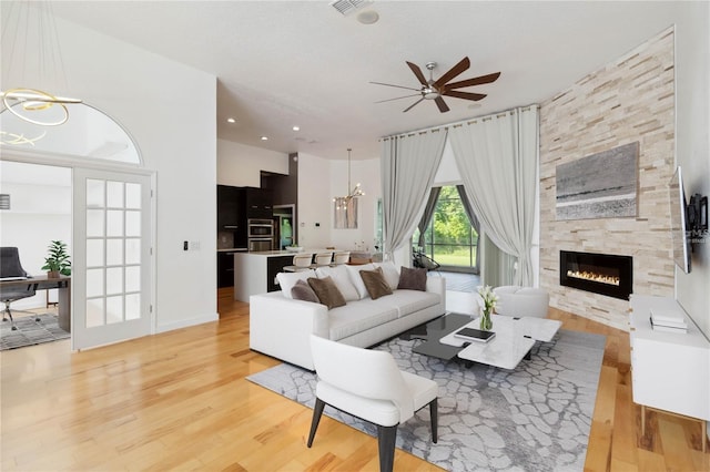 living room with light wood-type flooring, a fireplace, and ceiling fan with notable chandelier