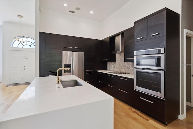 kitchen with wall chimney exhaust hood, modern cabinets, appliances with stainless steel finishes, light countertops, and a sink