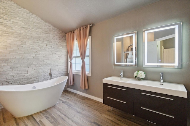 bathroom with double vanity, a sink, a freestanding bath, and wood finished floors