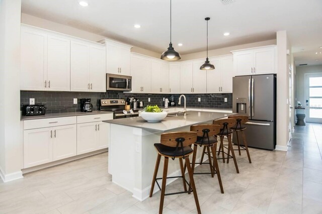 kitchen featuring a kitchen island with sink, stainless steel appliances, a breakfast bar, a sink, and white cabinetry