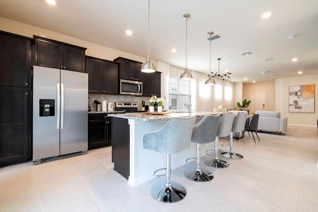 kitchen featuring tasteful backsplash, visible vents, appliances with stainless steel finishes, a breakfast bar, and light stone countertops