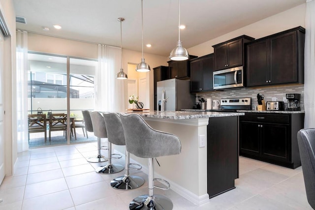 kitchen with tasteful backsplash, a center island with sink, visible vents, appliances with stainless steel finishes, and light stone counters