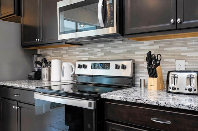 kitchen featuring dark brown cabinets, appliances with stainless steel finishes, light stone countertops, and decorative backsplash