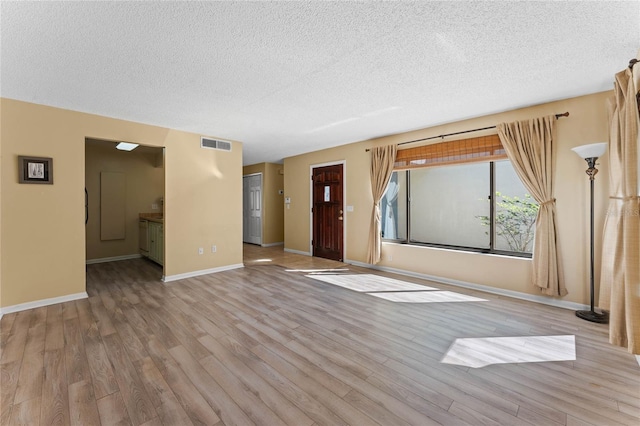 unfurnished living room with visible vents, a textured ceiling, baseboards, and wood finished floors