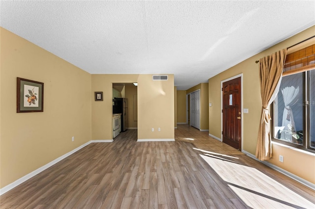 unfurnished living room featuring a textured ceiling, wood finished floors, visible vents, and baseboards