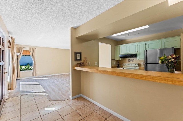 kitchen featuring range with electric cooktop, under cabinet range hood, freestanding refrigerator, green cabinetry, and light tile patterned floors